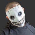 A person wearing a creepy, wide-grinning white mask with black cracks, hollow black eyes, and a sharp toothy grin, paired with a dark gray hoodie against a dark gray background.